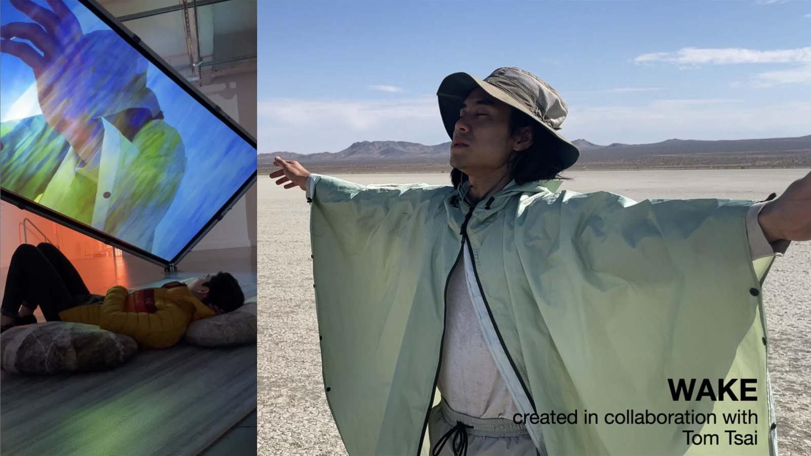 A male person stretches their arms out with a rain parka and a sun hat on in a desert like environment with their eyes closed